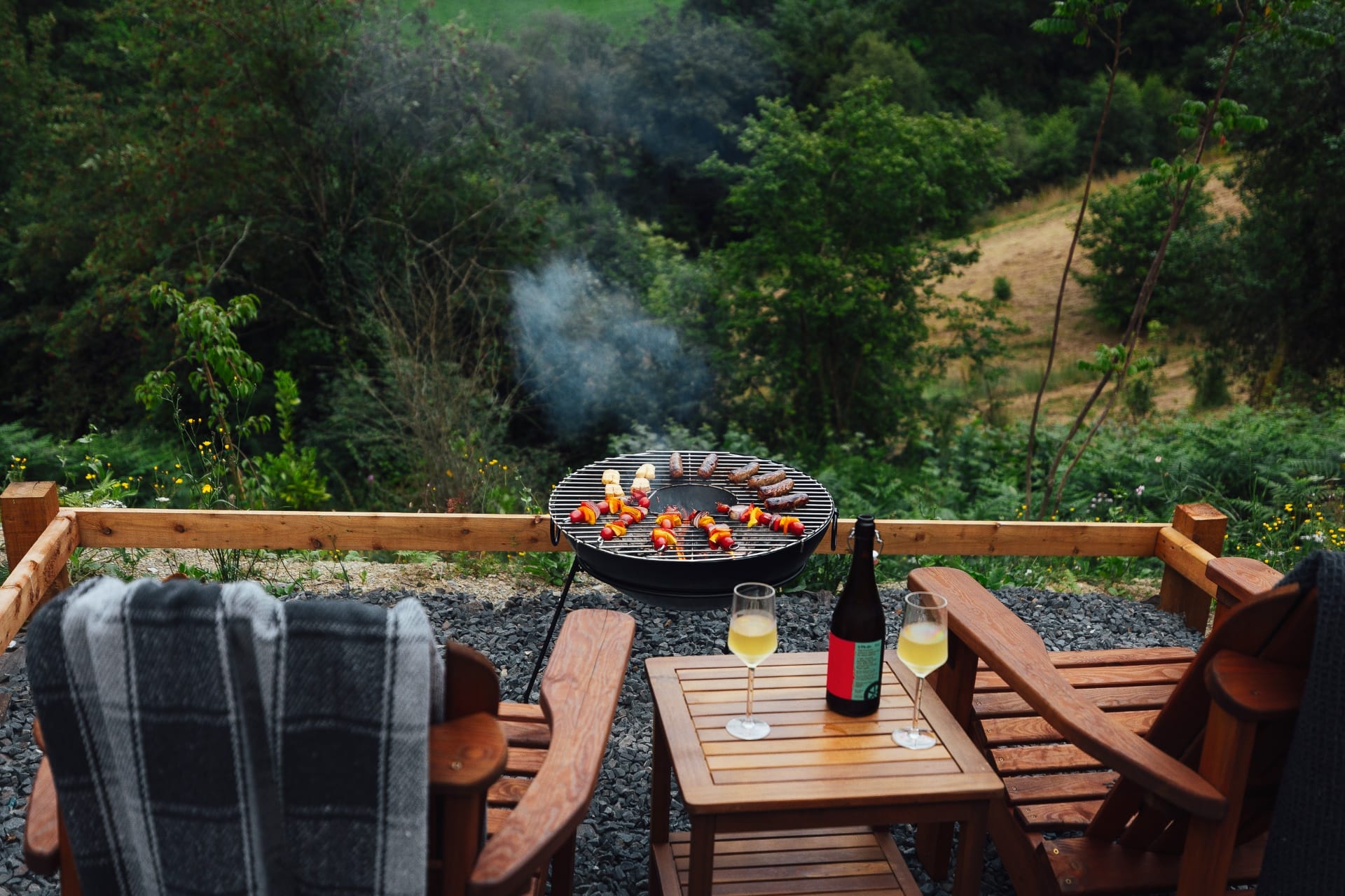 Fire pit with skewers grilling and Adirondack chairs above the valley