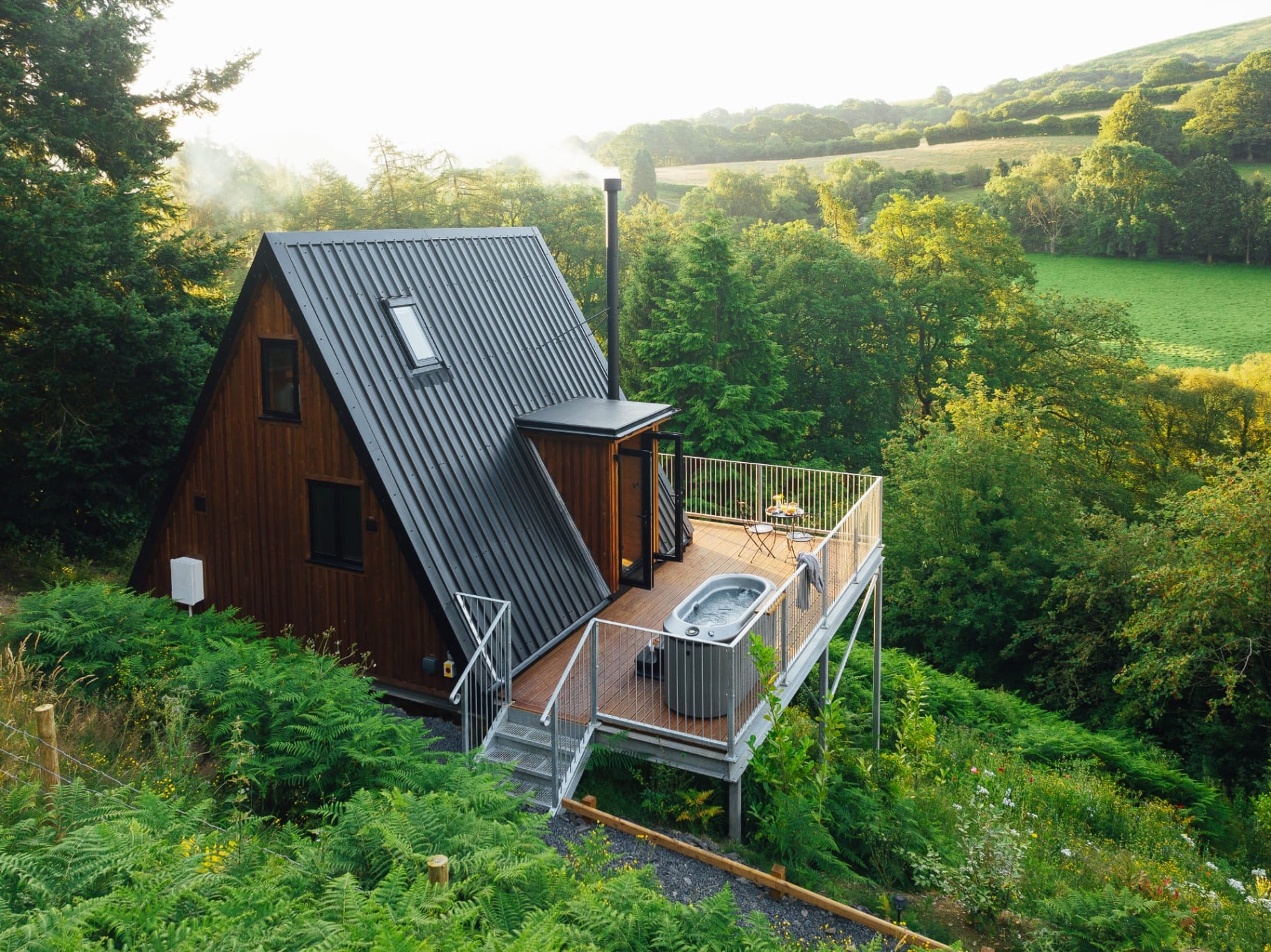 Aerial view of the A-frame cabin, deck and hot tub set among ferns and woodland