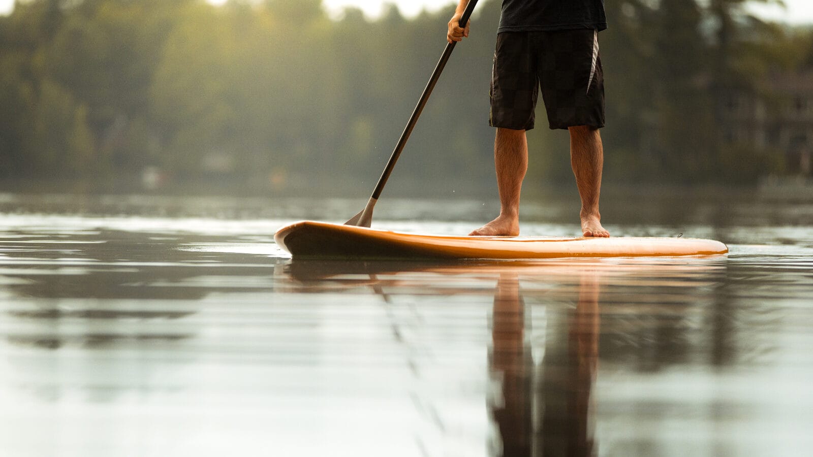 Paddleboarder gliding across a still mid Wales lake at sunrise